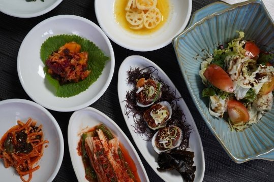 위에서 본 반찬 — 연근, 조개 껍데기에 올린 양념 찬과 해초, 토마토 샐러드, 김치